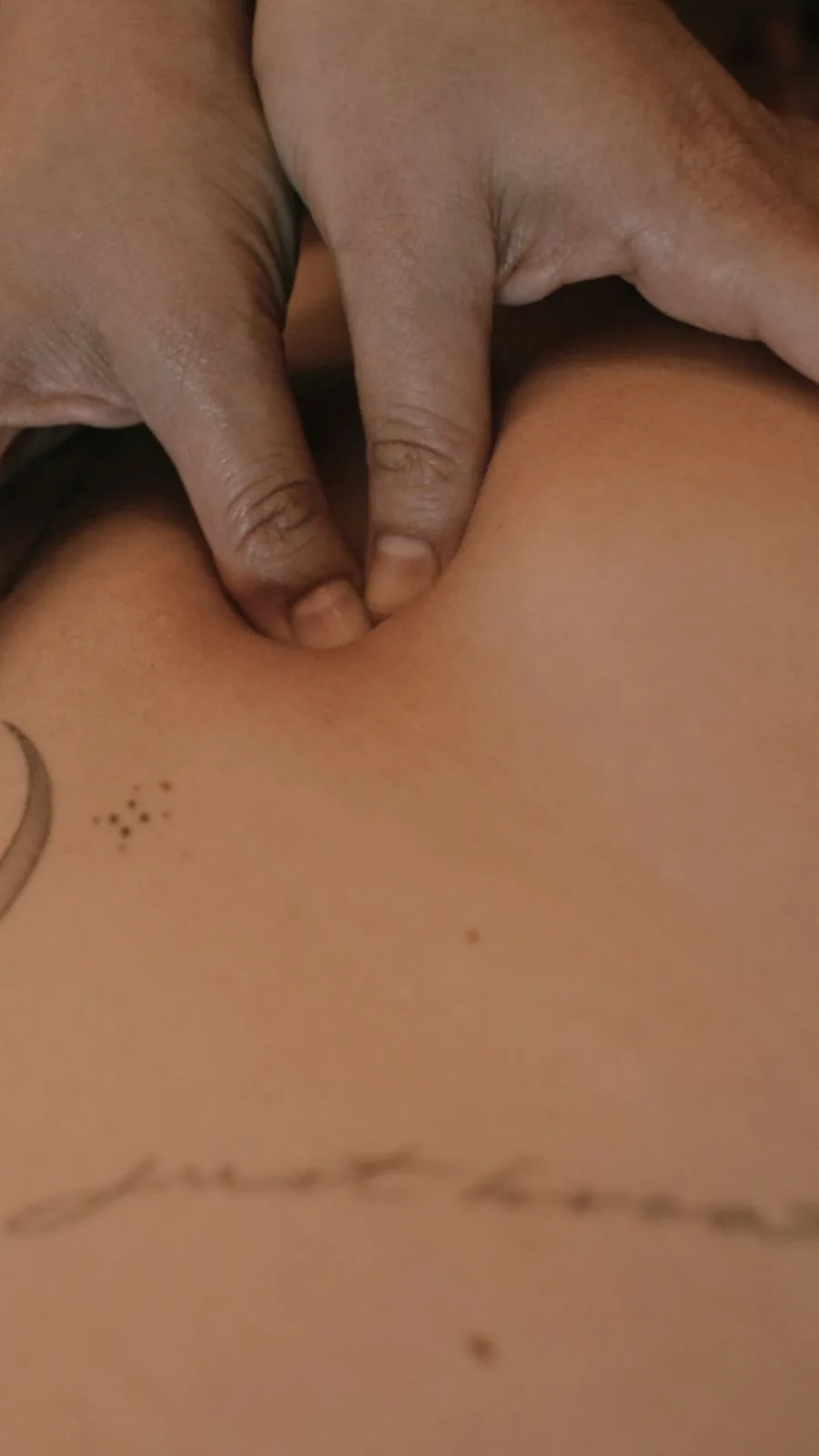 Primo piano sulle dita della massoterapista che premono su un punto preciso della schiena, vicino a un piccolo tatuaggio.